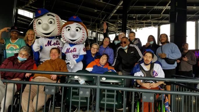 A group of intellectually and developmentally disabled adults attending a Mets game in New York City sitting with Mr. and Mrs. Met.