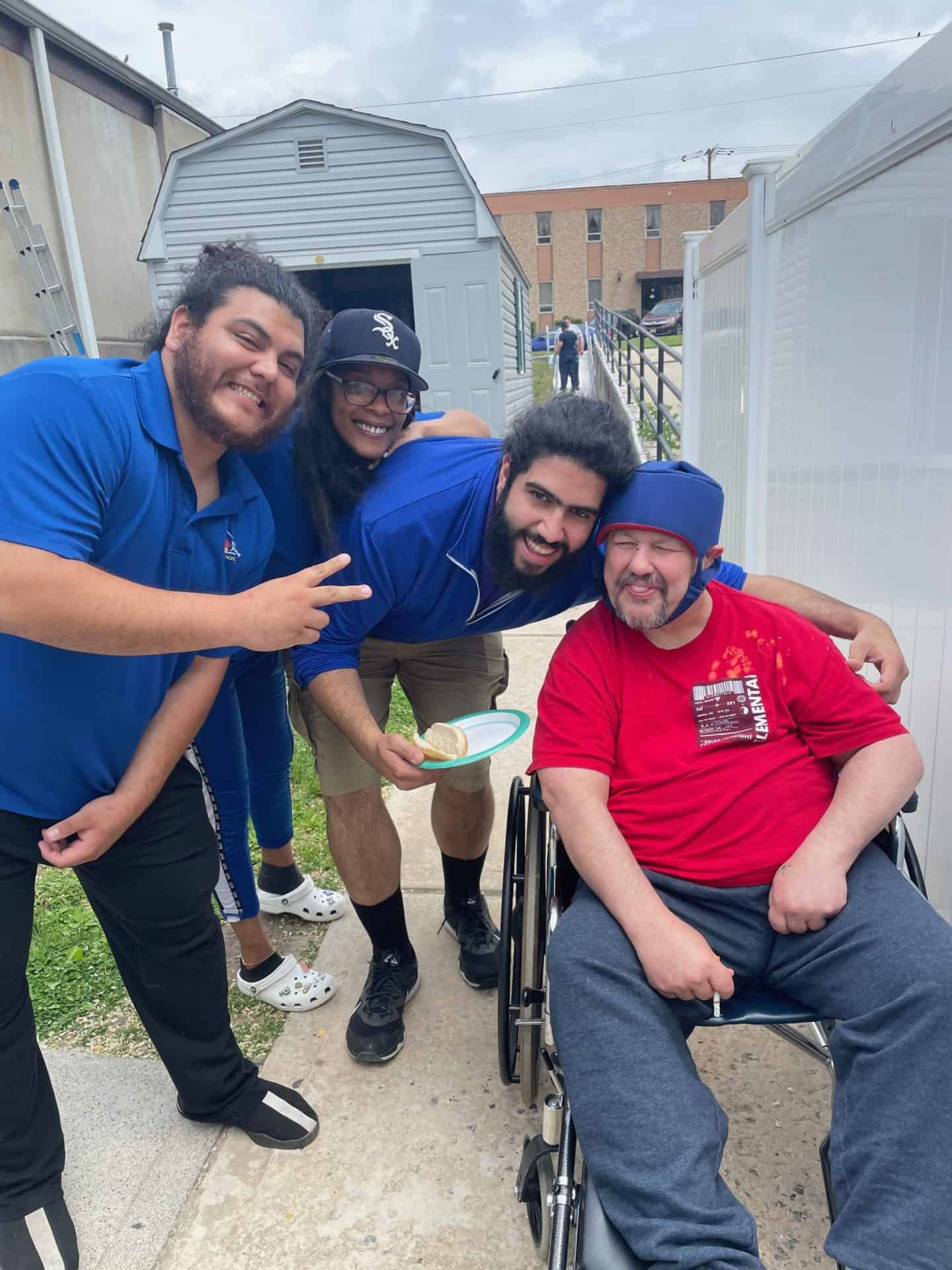 Three NCFL staff members and one resident in a wheelchair smiling and laughing at the Memorial Day Cookout.
