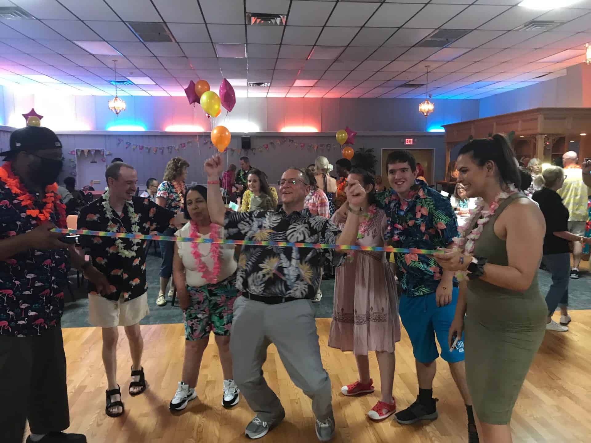  A group of people in Hawaiian shirts laughing and having fun doing the limbo with balloons in the background.